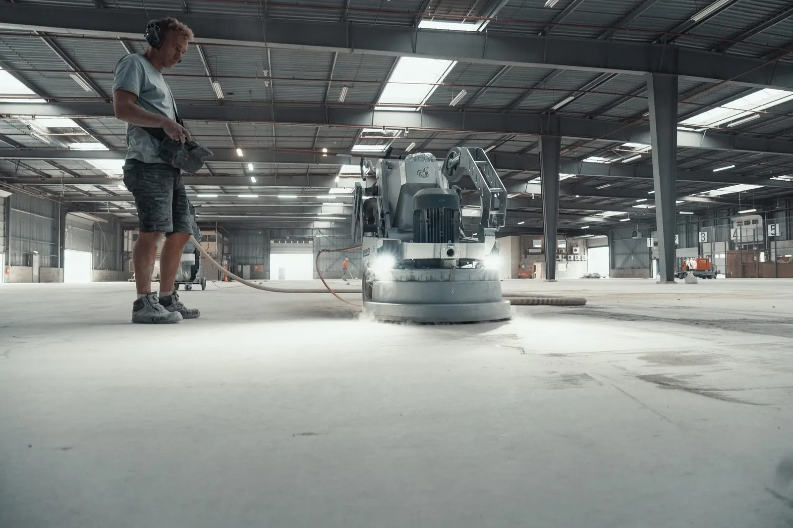 Vakman schuurt een betonvloer in een bedrijfshal met een professionele schuurmachine met stofafzuiging