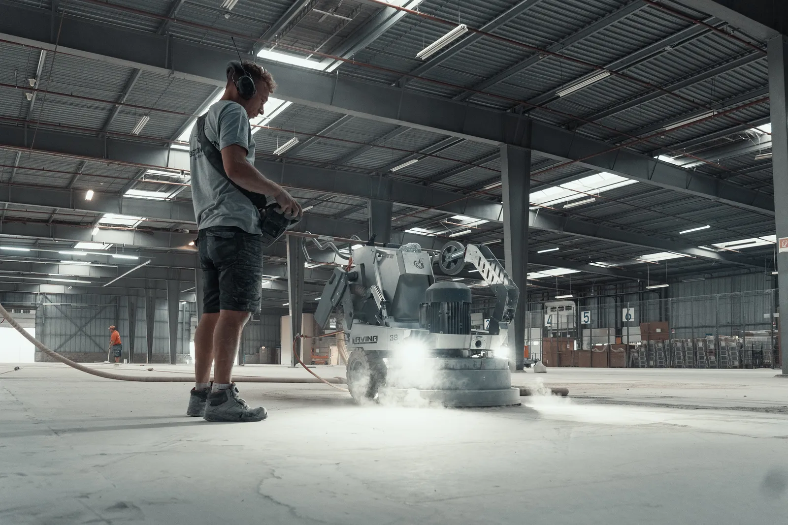 Vakman van Beton Design schuurt een betonvloer in een magazijn met een diamantschuurmachine